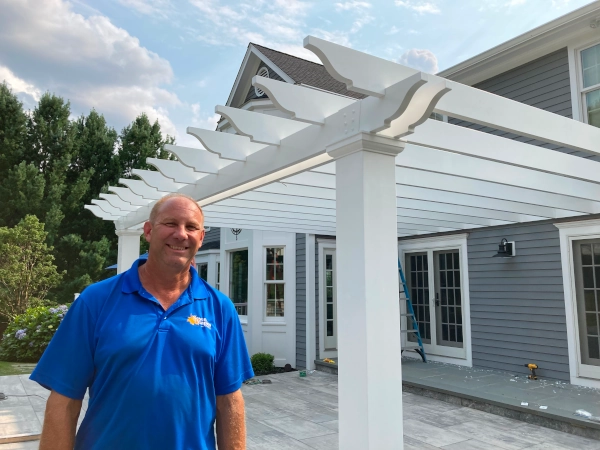 A beautiful white pergola attached to a gray house