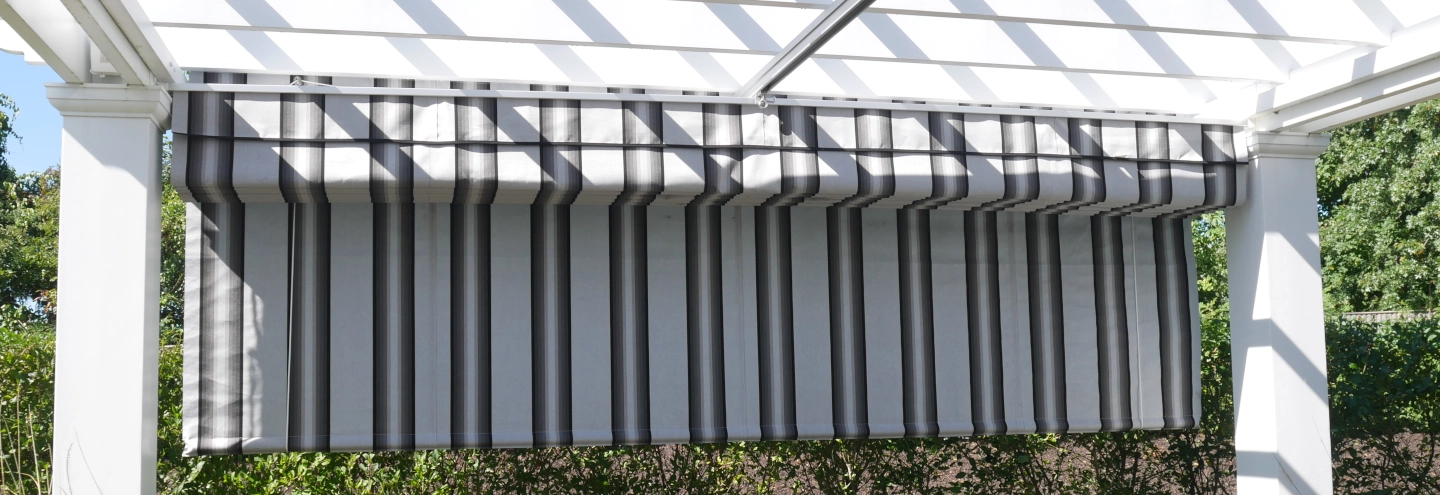 A pergola with a striped fabric roll-up shade